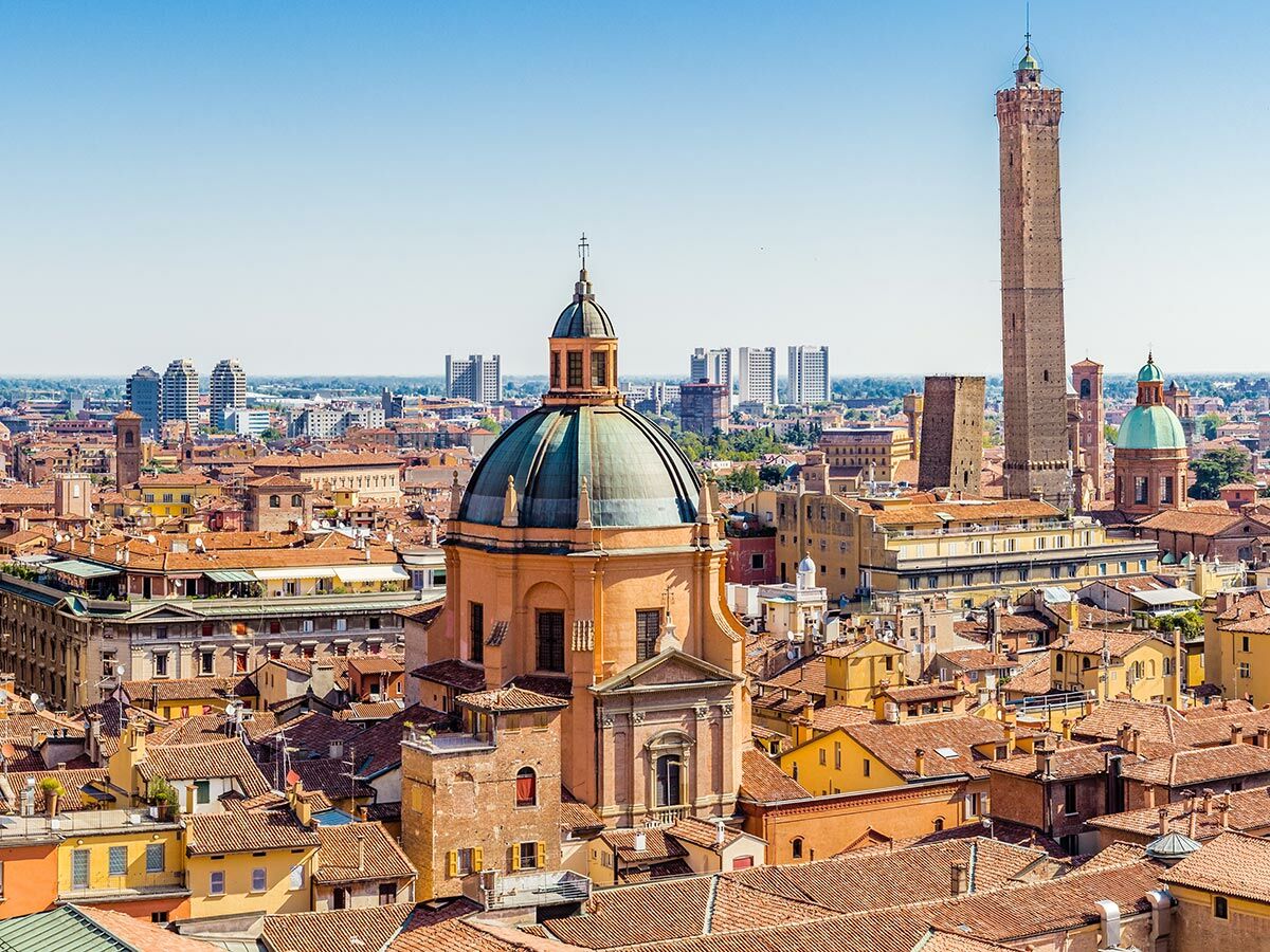 Panoramablick auf Bologna, Italien, mit roten Dächern, historischer Kuppel, Asinelli-Turm und Garisenda-Turm bei Sonnenschein.