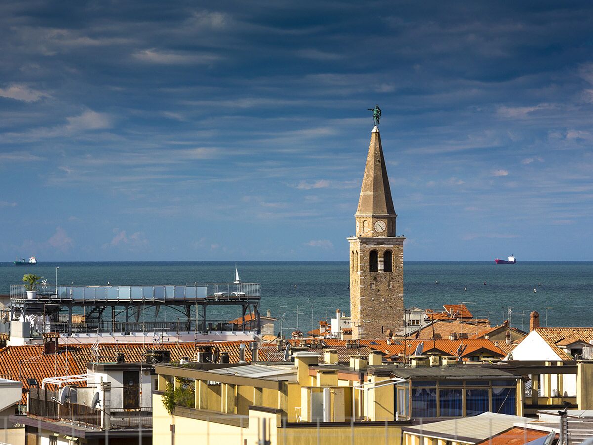Panoramablick auf die Küstenstadt Chioggia mit historischem Glockenturm, roten Dächern und dem Adriatischen Meer unter blauem Himmel.