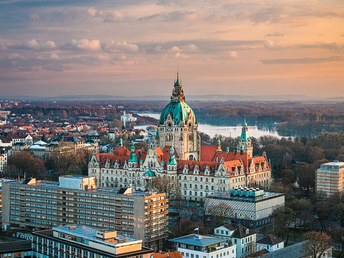 Panoramablick auf das Neue Rathaus in Hannover mit grüner Kuppel bei Sonnenuntergang, umgeben von Stadt und Maschsee.