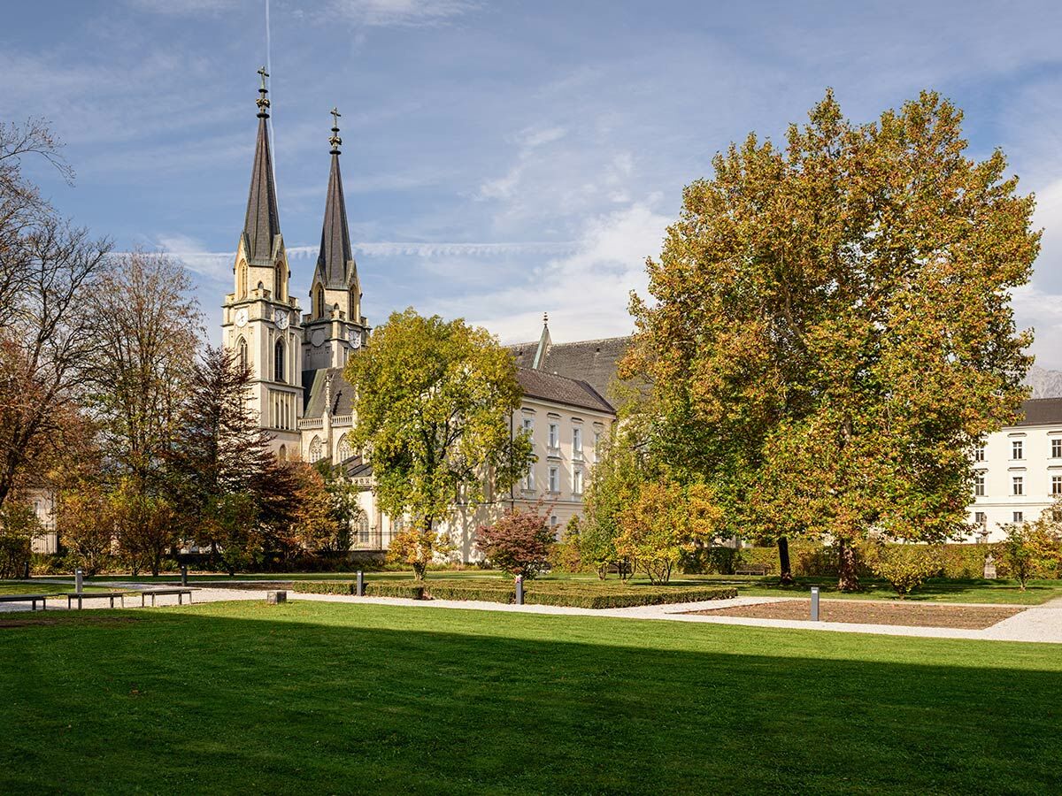 Historische Klosterkirche mit zwei spitzen Türmen, eingebettet in einen farbenprächtigen Park mit herbstlichen Bäumen und grünem Rasen.