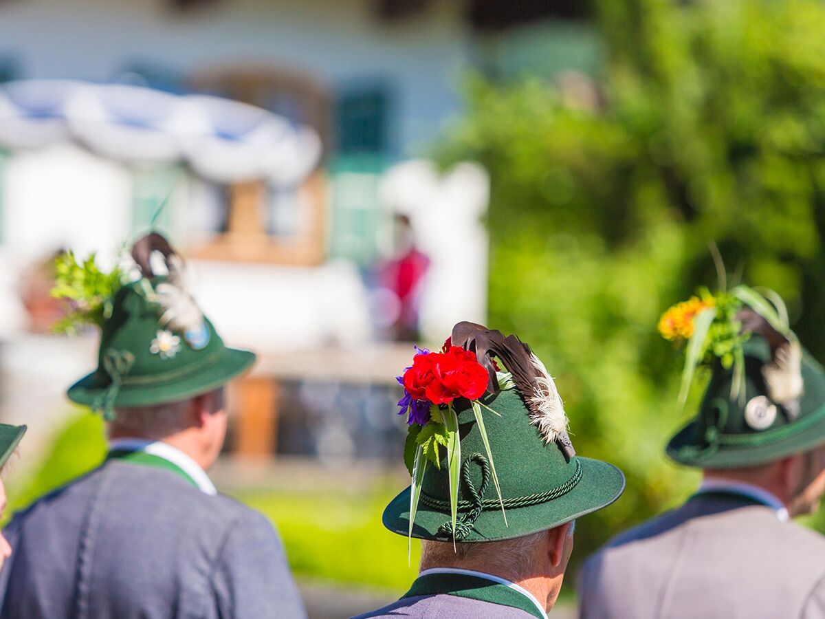 Rückenansicht von Männern mit traditionellen grünen Trachtenhüten, geschmückt mit Gamsbart, Federn und bunten Blumen.