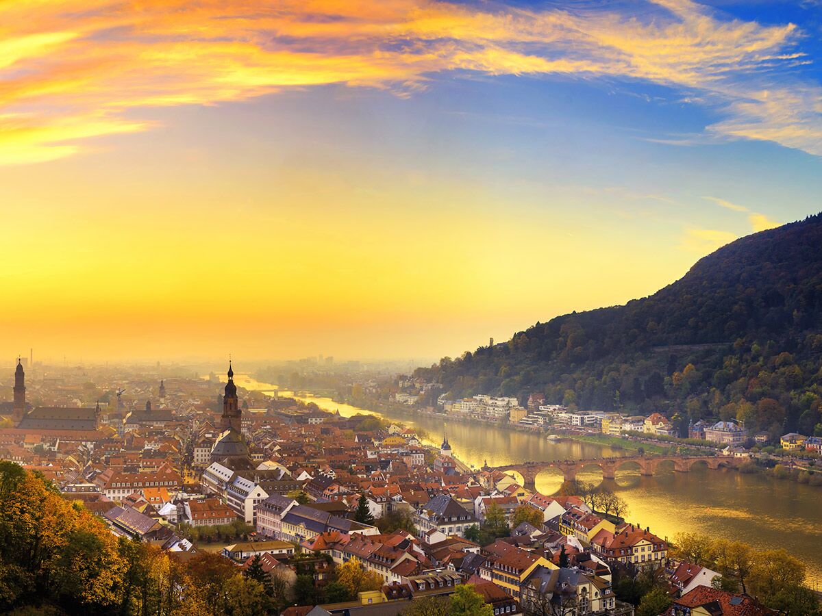 Goldener Sonnenuntergang über Heidelbergs Altstadt, Neckarfluss, Alter Brücke und Königstuhl. Historische Architektur im warmen Licht.