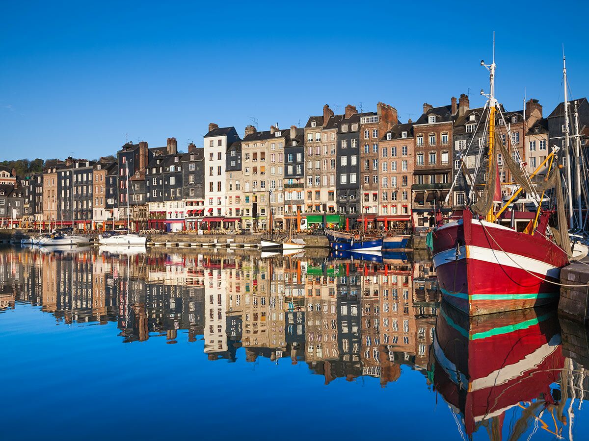 Malerischer Hafen von Honfleur in der Normandie mit bunten Gebäuden, Fischerbooten und klarem Wasser, das alles widerspiegelt.
