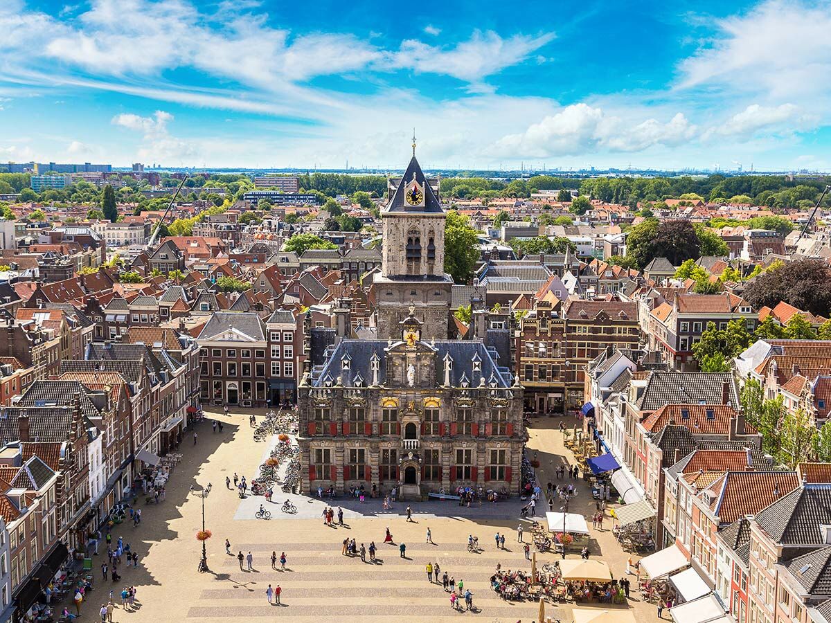 Luftaufnahme des Marktplatzes in Delft, Niederlande, mit dem historischen Rathaus, der Nieuwe Kerk und belebten Menschenmengen.