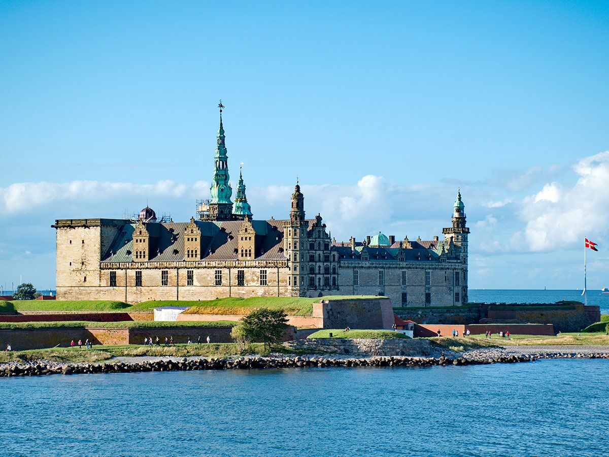 Historisches Kronborg Schloss mit grünen Türmen an der Küste Dänemarks unter blauem Himmel am Meer.