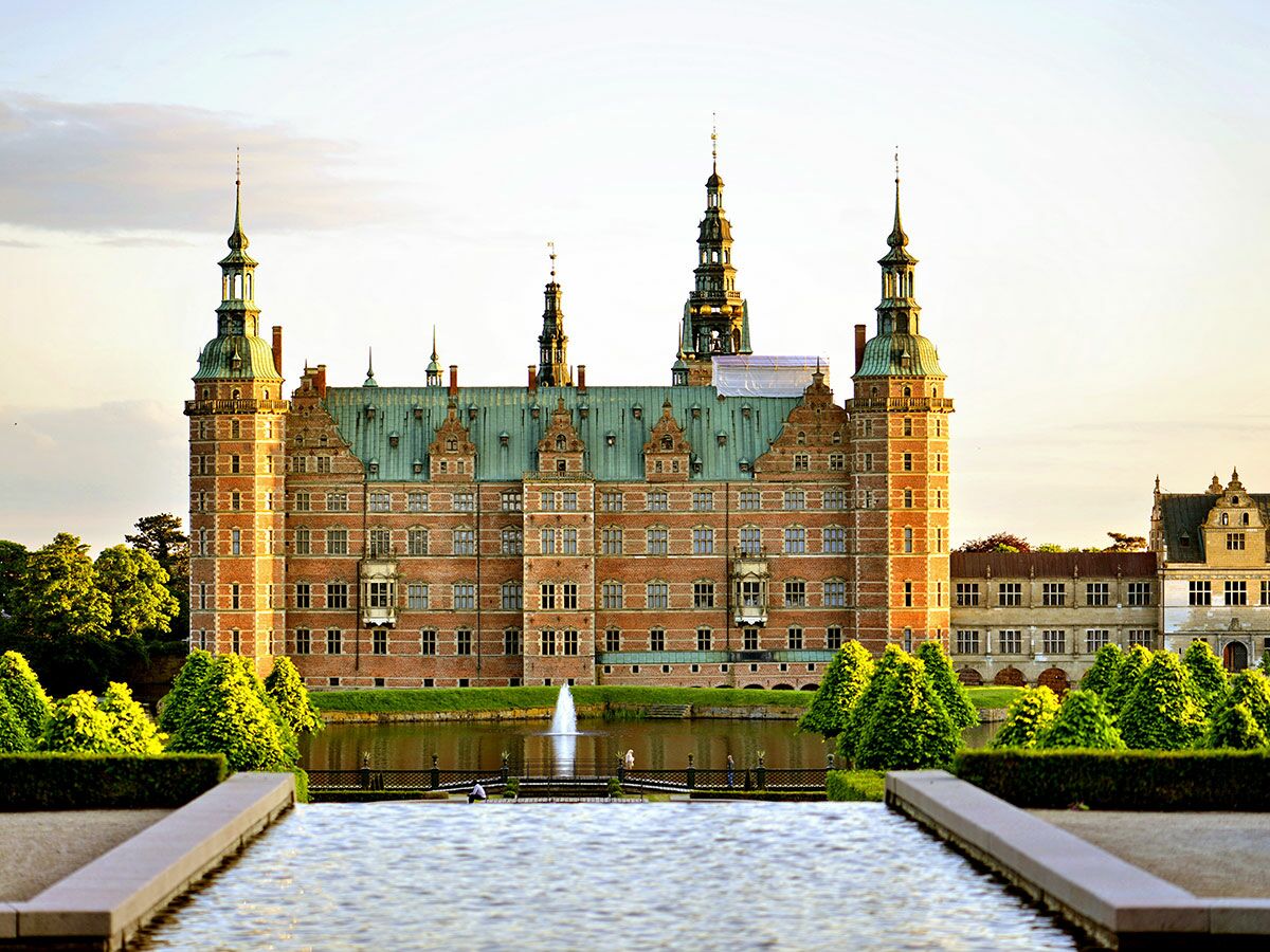 Majestätisches Frederiksborg Schloss in Hillerød, Dänemark, mit roten Backsteinmauern, grünen Kupferdächern, See und Gärten bei Sonnenuntergang.