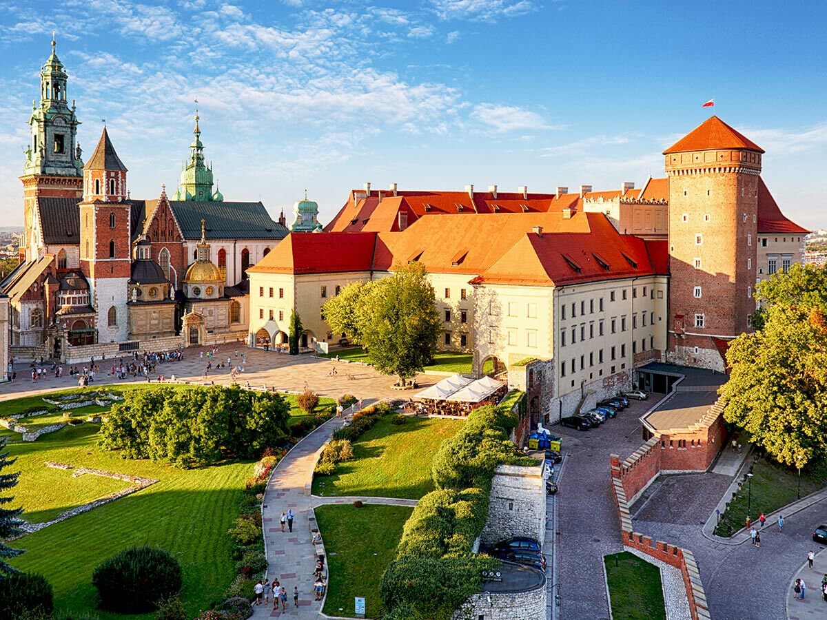 Panoramablick auf das Wawel Schloss und die Kathedrale in Krakau, Polen, mit roten Dächern und grünen Gärten unter blauem Himmel.