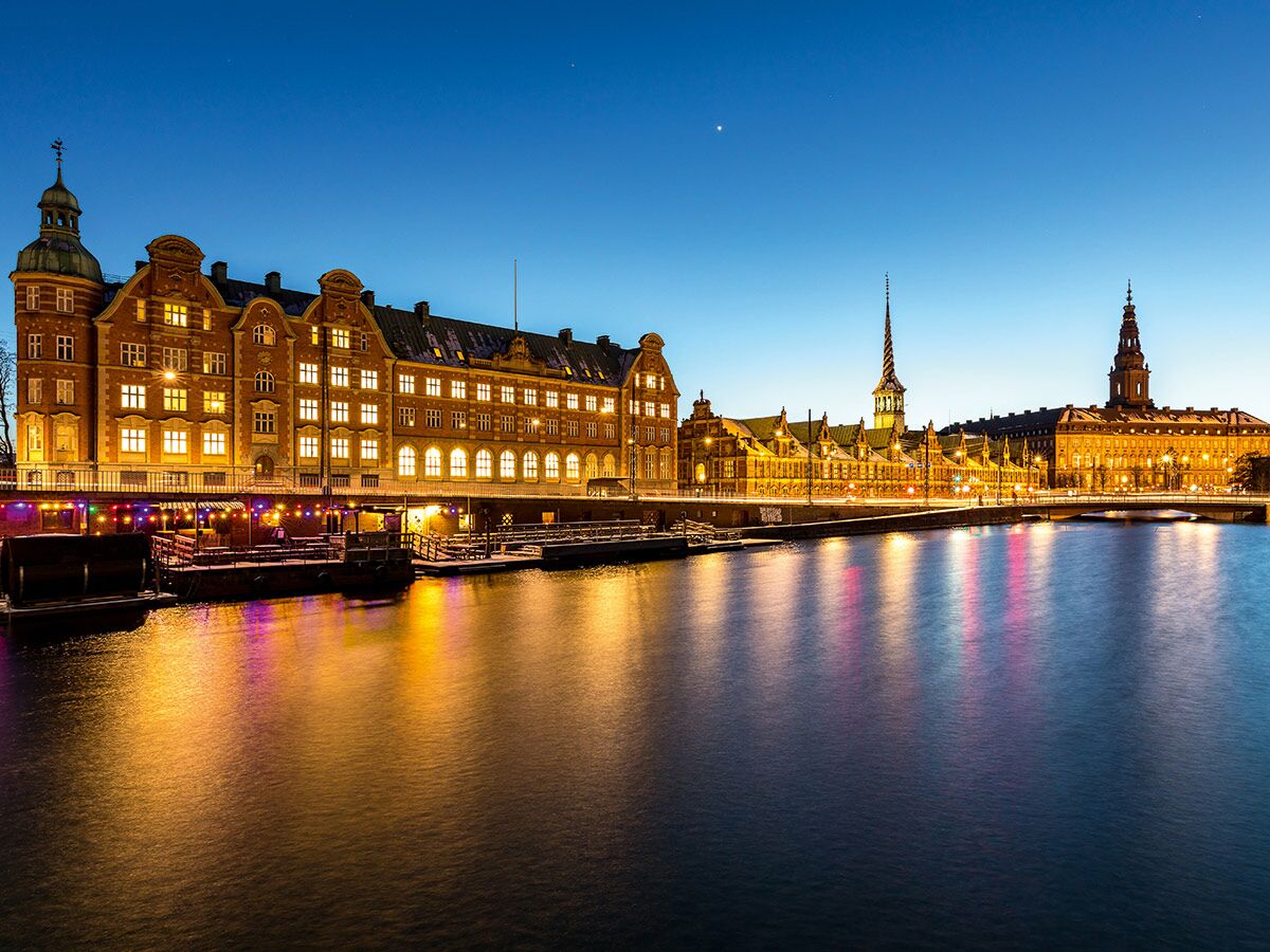 Kopenhagen Abendblick mit historischen Gebäuden, Børsen-Turm, Brücke und Wasserreflexionen im blauen Licht.