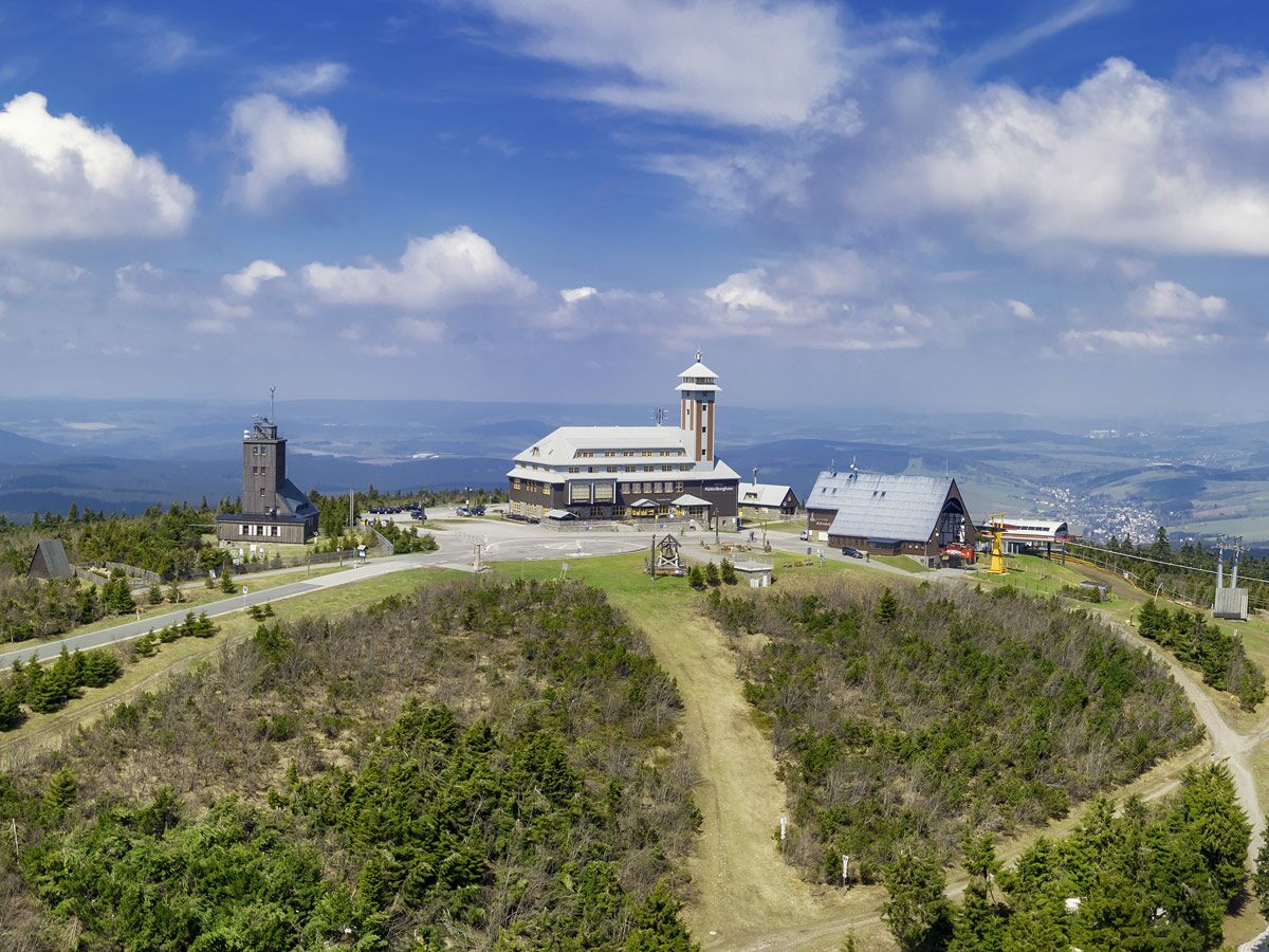Der Brocken-Gipfel im Harz mit historischen Gebäuden, Funkturm und Hotel unter blauem Himmel, umgeben von Wald und weitem Ausblick.