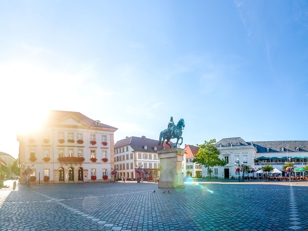 Sonnenbeschienener Marktplatz in Bad Ems mit Reiterstatue von Kaiser Wilhelm I., historischen Gebäuden und Außengastronomie unter blauem Himmel.