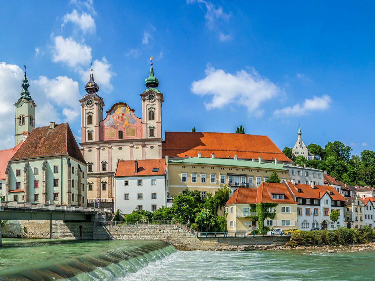 Panoramablick auf Lechbruck am See mit der Pfarrkirche Mariä Himmelfahrt und bunten Gebäuden am Fluss Lech unter blauem Himmel.