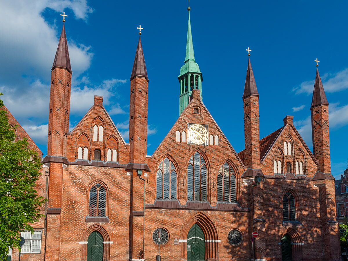Historische Backsteingotik Kirche mit roten Ziegeln, hohen Türmen, Bogenfenstern und Uhr unter blauem Himmel in Lübeck.