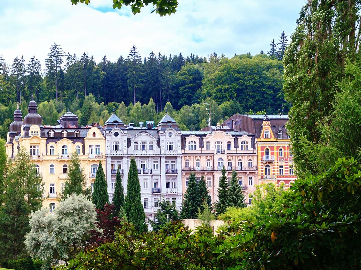 Bunte historische Gebäude eines Kurortes vor dichtem Waldhintergrund, Karlovy Vary, Tschechien, sonniger Tag.