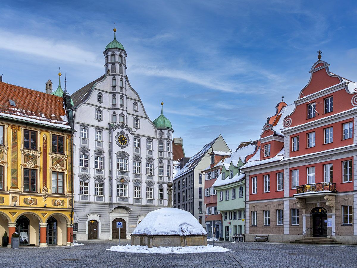Winterlicher Marktplatz Landsberg am Lech mit historischem Rathaus, bunten Gebäuden und Brunnen unter blauem Himmel.