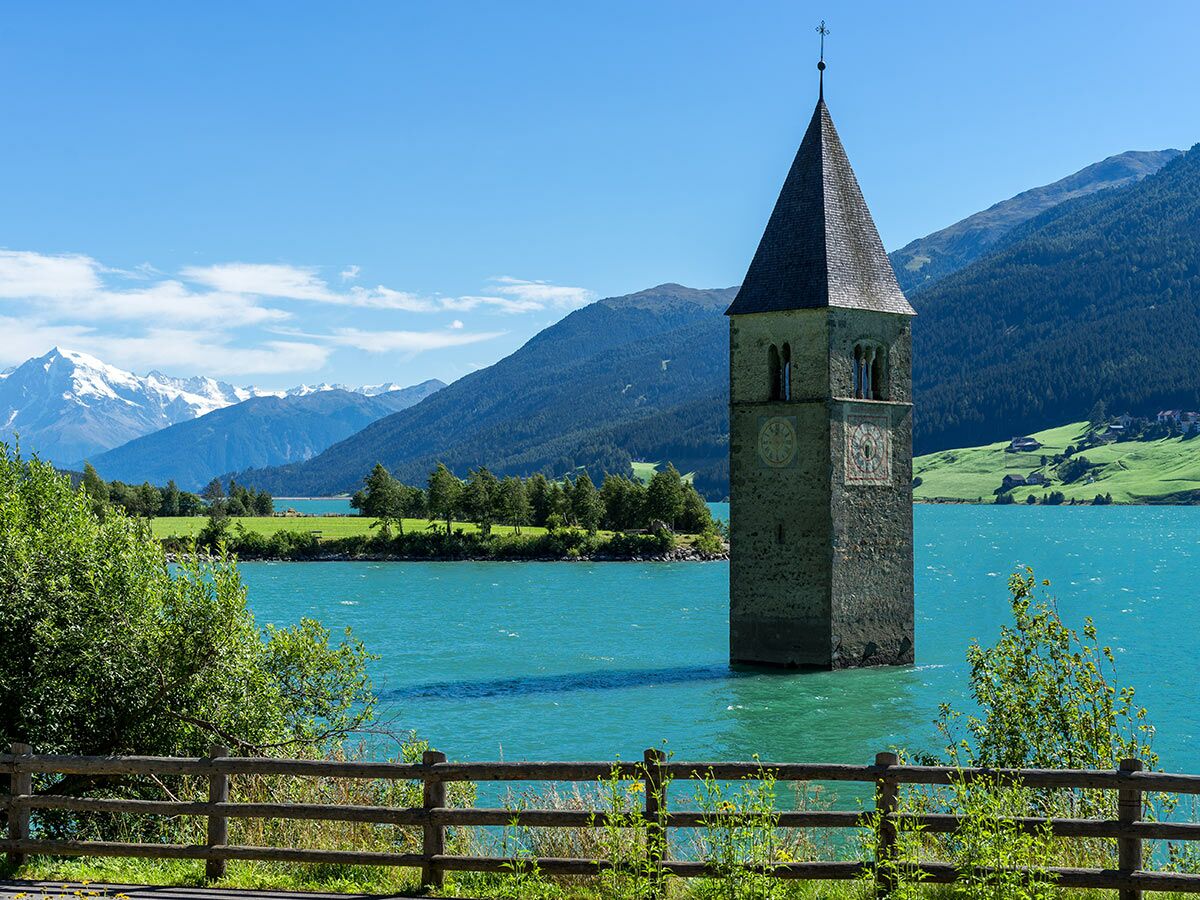 Der berühmte versunkene Kirchturm im Reschensee, Südtirol, mit türkisblauem Wasser und schneebedeckten Alpen im Hintergrund.