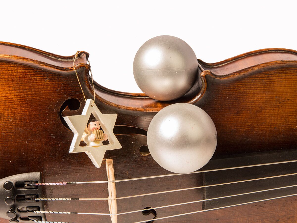 Nahaufnahme einer braunen Violine, geschmückt mit silbernen Weihnachtskugeln und einem sternförmigen Engel-Ornament.
