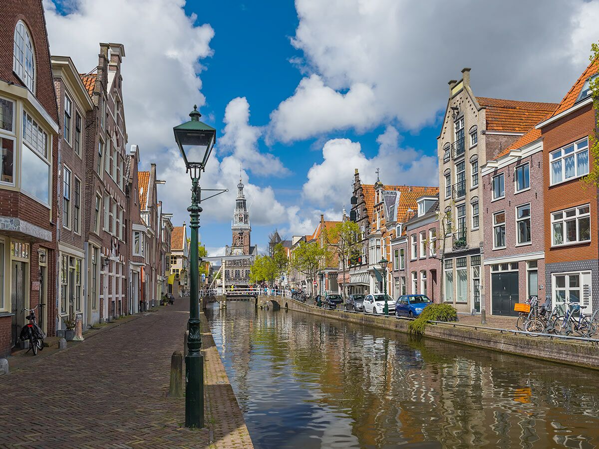 Blick auf eine historische Gracht in Alkmaar, Niederlande, mit Giebelhäusern, dem Waagturm und blauem Himmel.