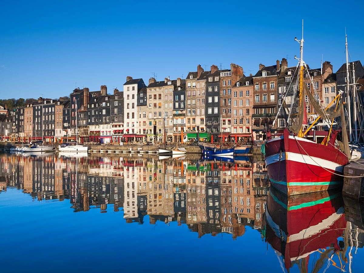 Historischer Hafen von Honfleur, Frankreich, mit bunten Gebäuden und Fischerbooten, die sich im ruhigen Wasser spiegeln.