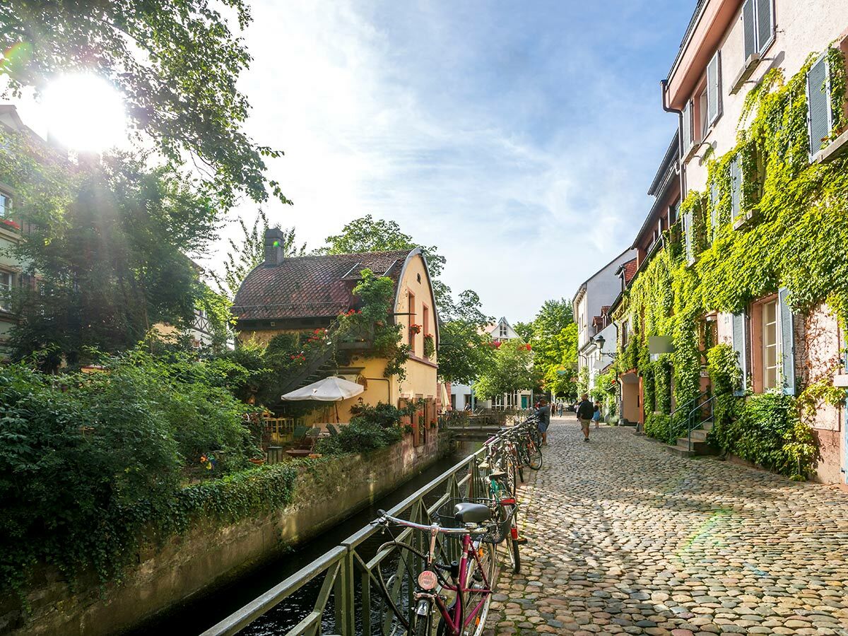 Charmante Gasse in europäischer Altstadt mit Kanal, historischen Häusern, üppigem Efeu, Kopfsteinpflaster und geparkten Fahrrädern.