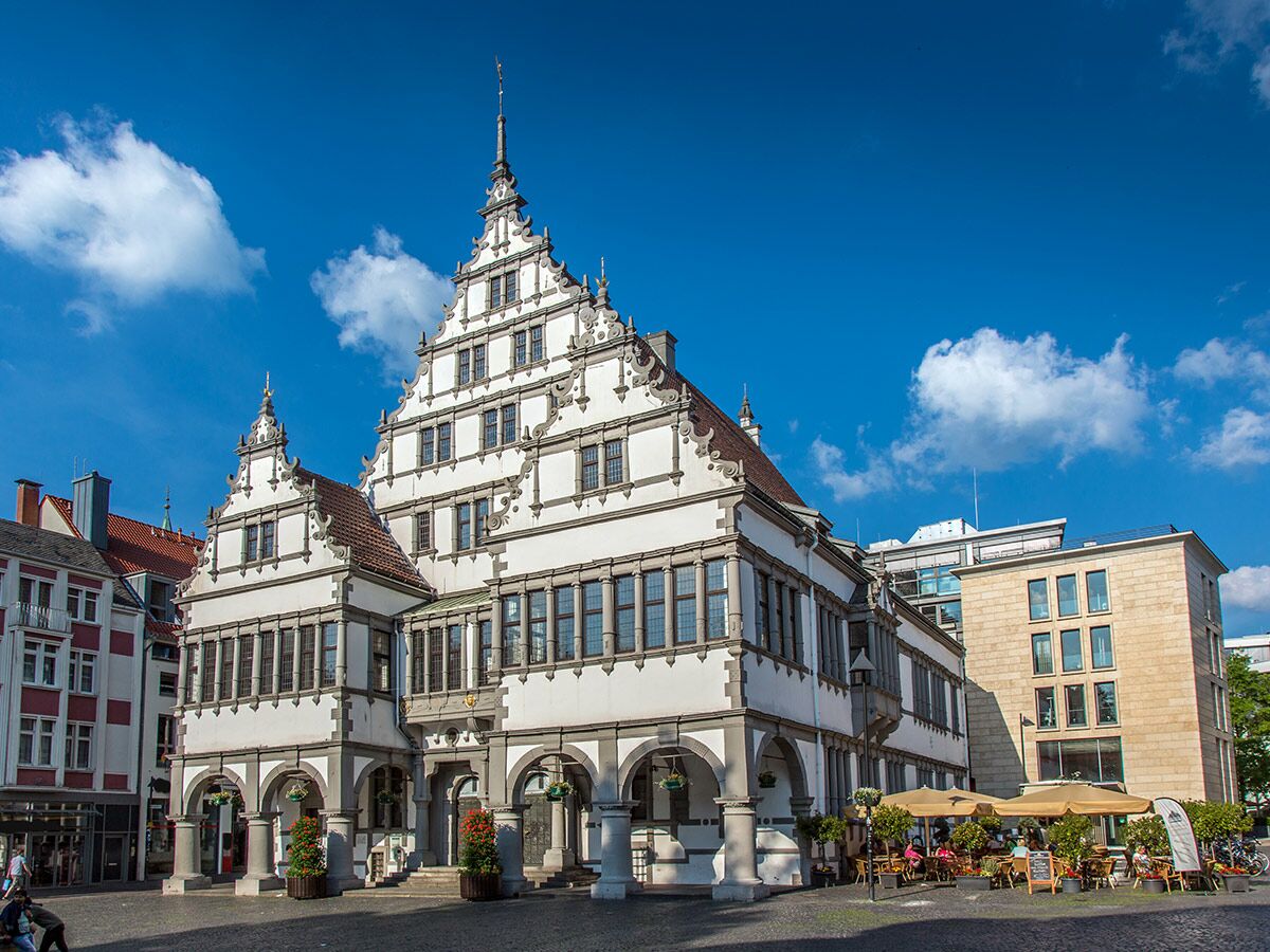 Historisches Rathaus Detmold in Deutschland mit markanten Giebeln, Arkaden und davorliegendem Marktplatz mit Außencafé bei Sonnenschein.