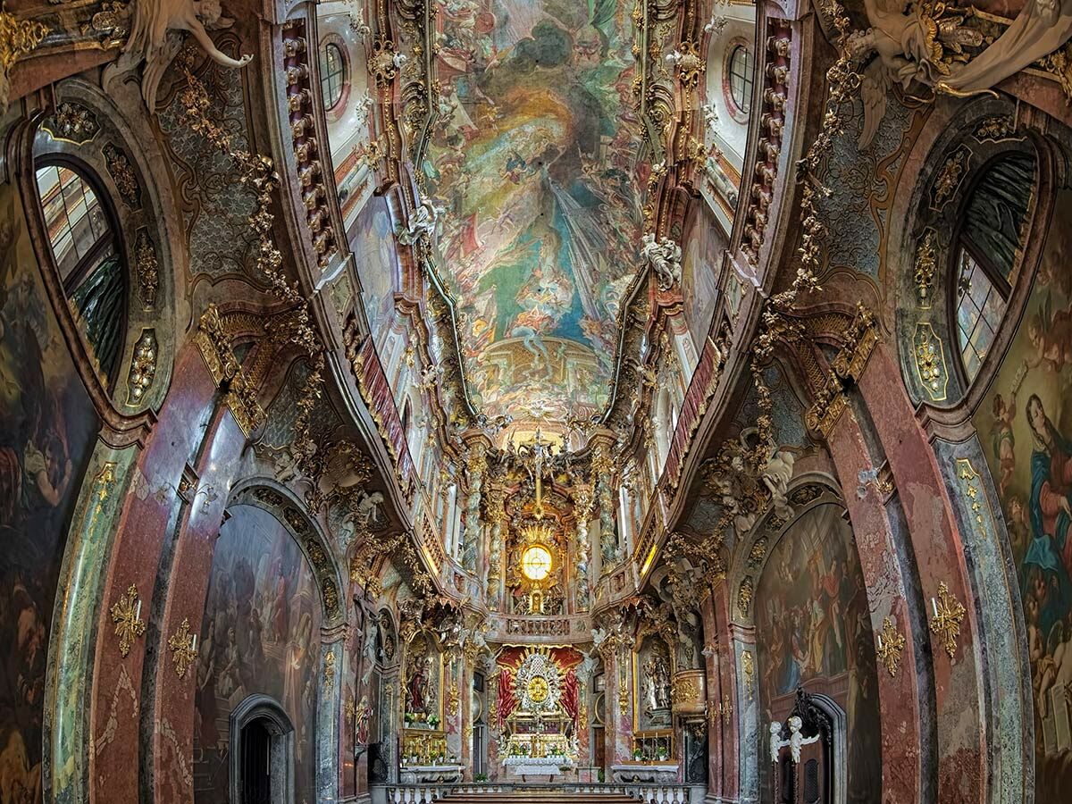Üppig verziertes barockes Kircheninneres mit farbenprächtigem Deckenfresko, goldenem Stuck, Marmorsäulen und Wandgemälden.