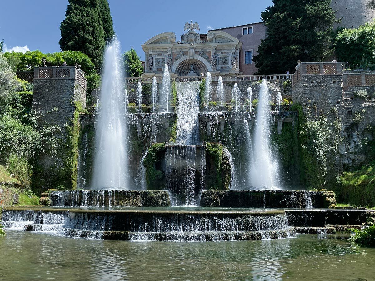 Großer mehrstufiger Brunnen mit vielen Wasserfällen vor einer historischen Villa in einem Garten in Tivoli, Italien.
