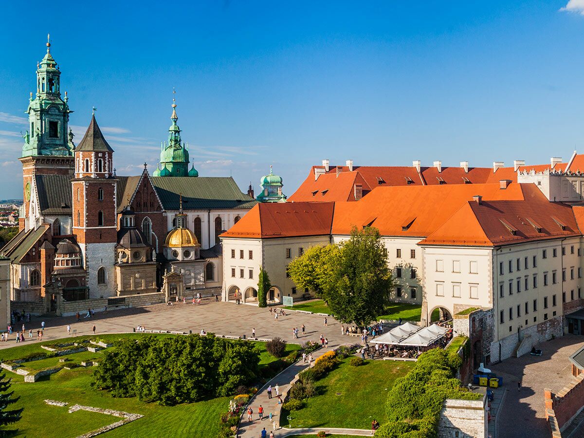Panoramablick auf die Wawel-Kathedrale und das Königsschloss in Krakau, Polen, mit grünen und orangefarbenen Dächern unter blauem Himmel.