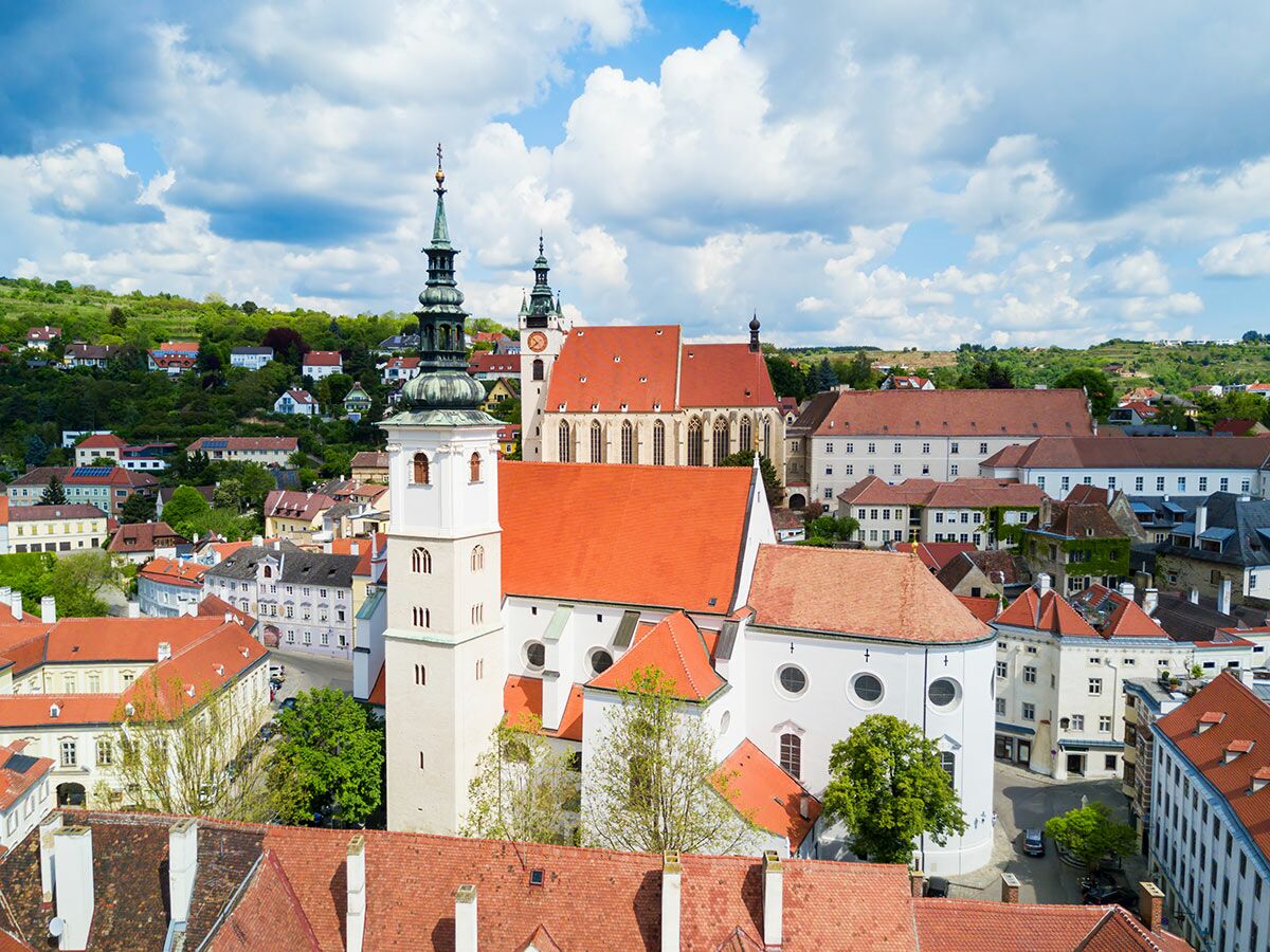 Luftaufnahme der historischen Altstadt von Krems an der Donau mit Piaristenkirche, Dominikanerkirche und roten Dächern unter blauem Himmel.