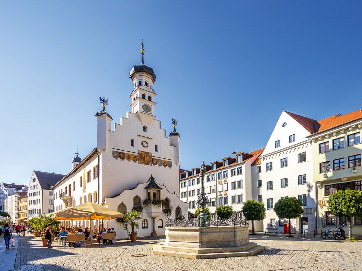 Historisches Rathaus mit Uhrturm am sonnigen Marktplatz einer europäischen Stadt mit Menschen im Straßencafé.
