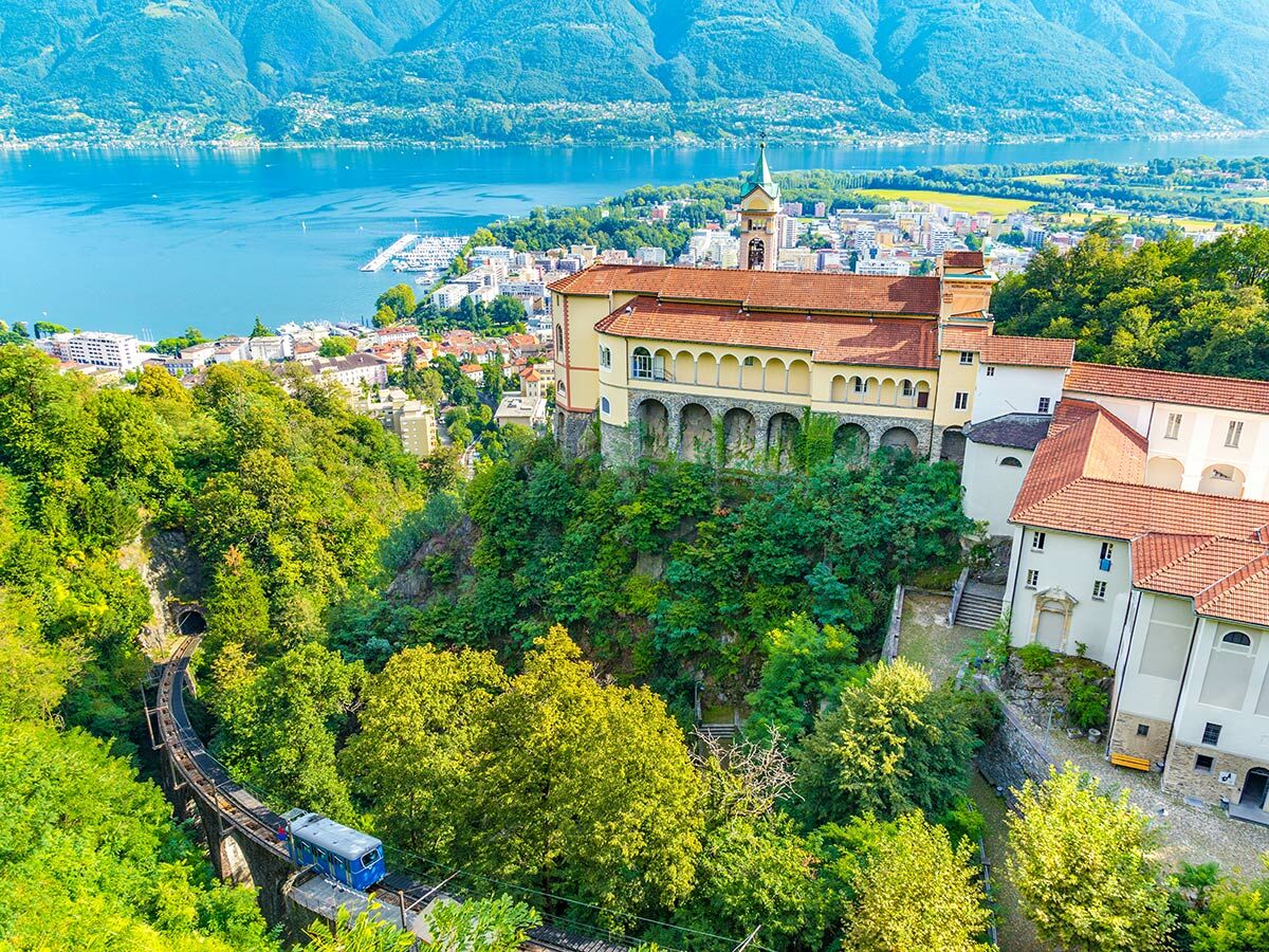 Luftaufnahme von Locarno mit Lago Maggiore, Bergen, Madonna del Sasso Heiligtum und der Standseilbahn durch grüne Landschaft.