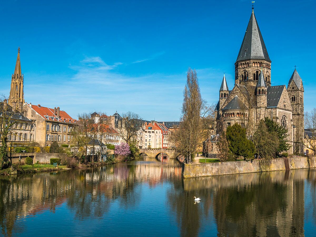 Metz Stadtansicht mit der protestantischen Kirche Temple Neuf an der Mosel, reflektiert im Wasser unter blauem Himmel.