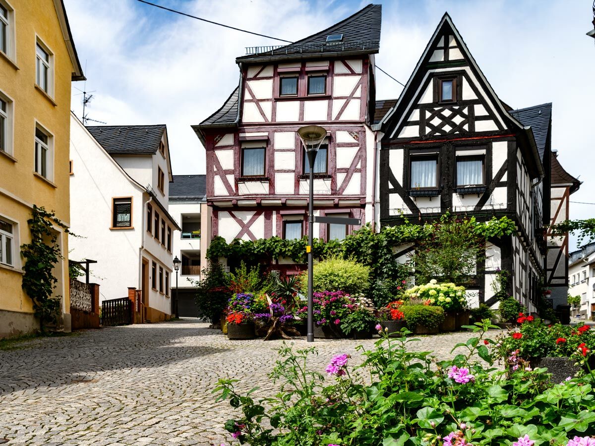 Idyllische Kopfsteinpflastergasse mit farbenfrohen Fachwerkhäusern und vielen blühenden Pflanzen in einer deutschen Stadt.