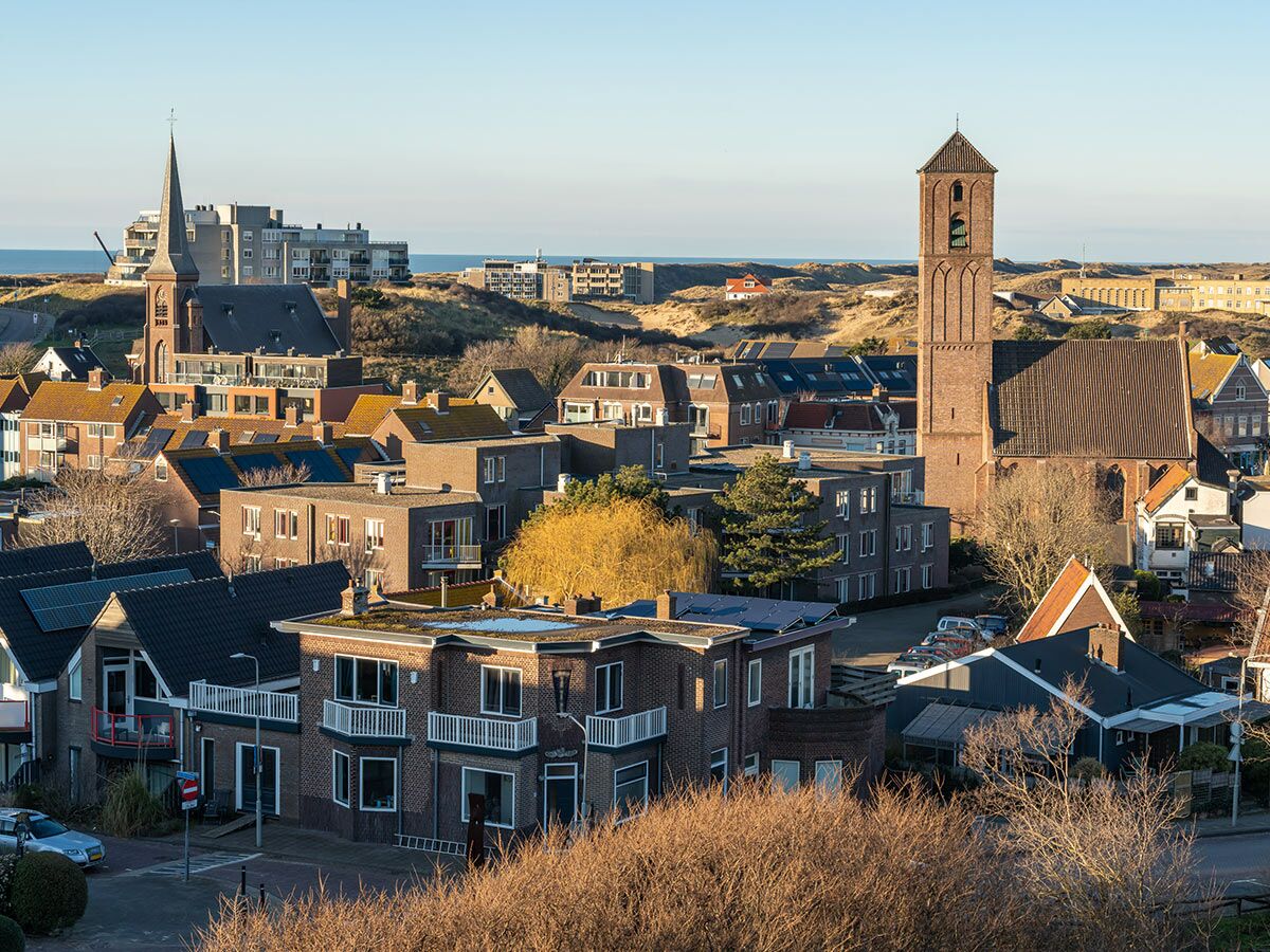 Panoramablick auf eine charmante Küstenstadt in den Niederlanden mit Häusern, Kirchen, Sanddünen und dem Meer im Hintergrund.