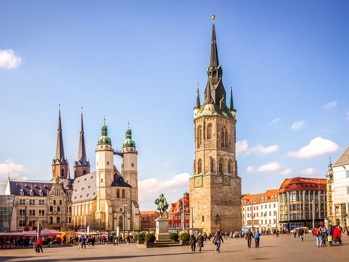 Blick auf den belebten Marktplatz in Halle (Saale) mit der Marktkirche, dem Roten Turm und vielen Passanten an einem sonnigen Tag.