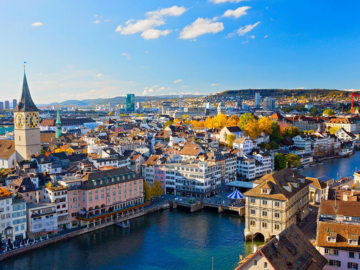 Luftaufnahme von Zürich, Schweiz, mit Limmat, Fraumünster-Glockenturm, historischen Altstadthäusern und Herbstbäumen unter blauem Himmel.